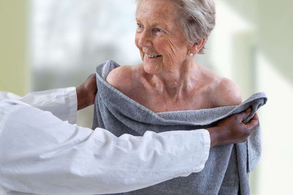 An elderly woman being handed a towel after taking a bath in an Apollo Bath bathing solution.