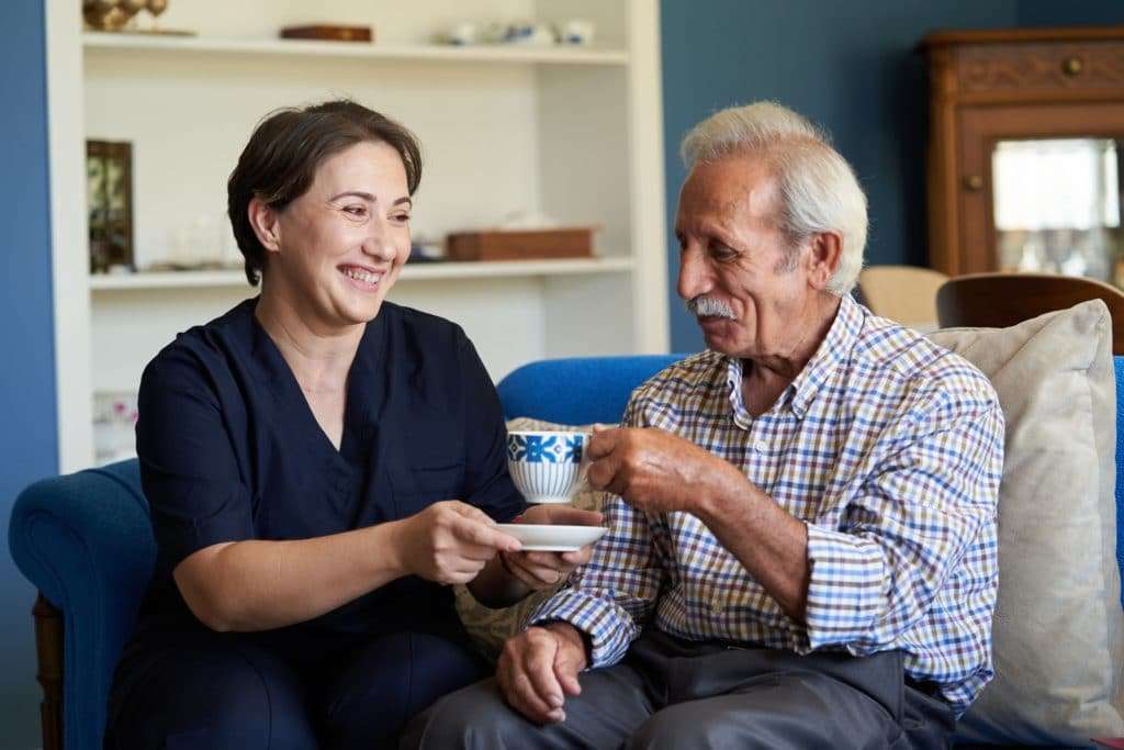 A nurse helping an old man drink tea.