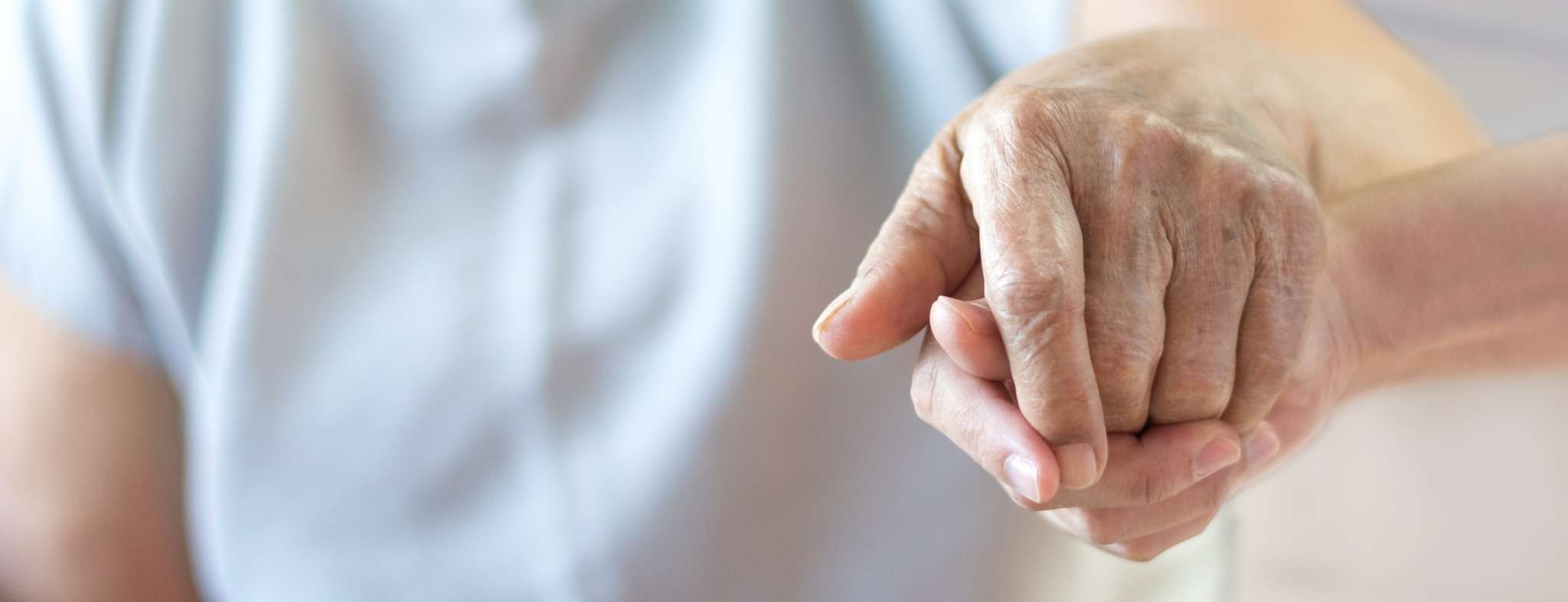 An eldery person holding hands with a caregiver.