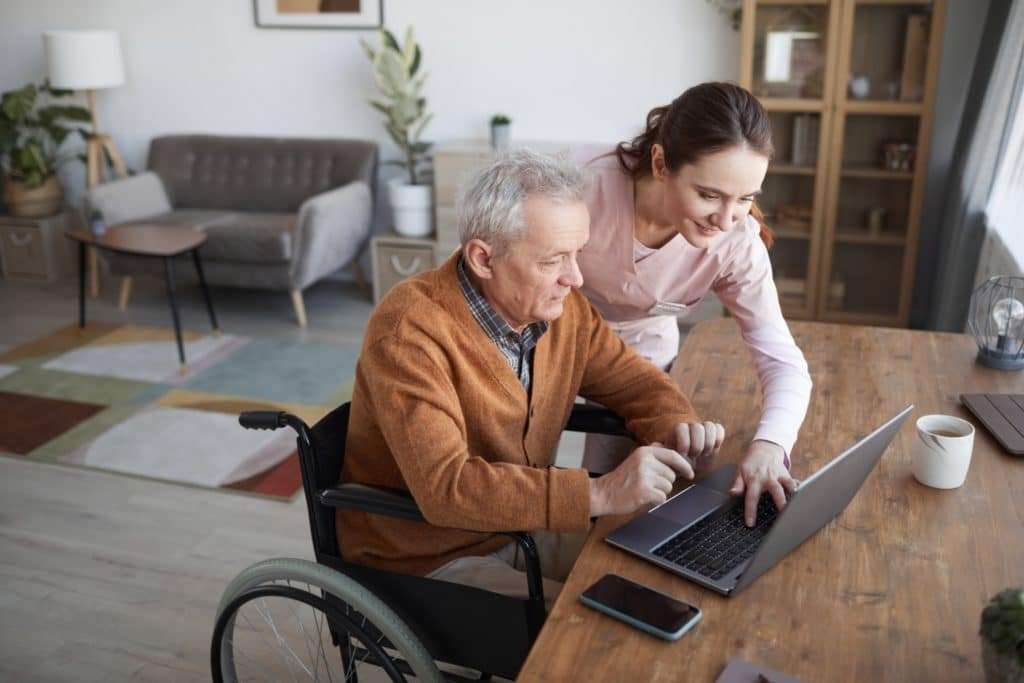 A long-term care nurse offering comapssionate care by helping an elderly man use a computer.