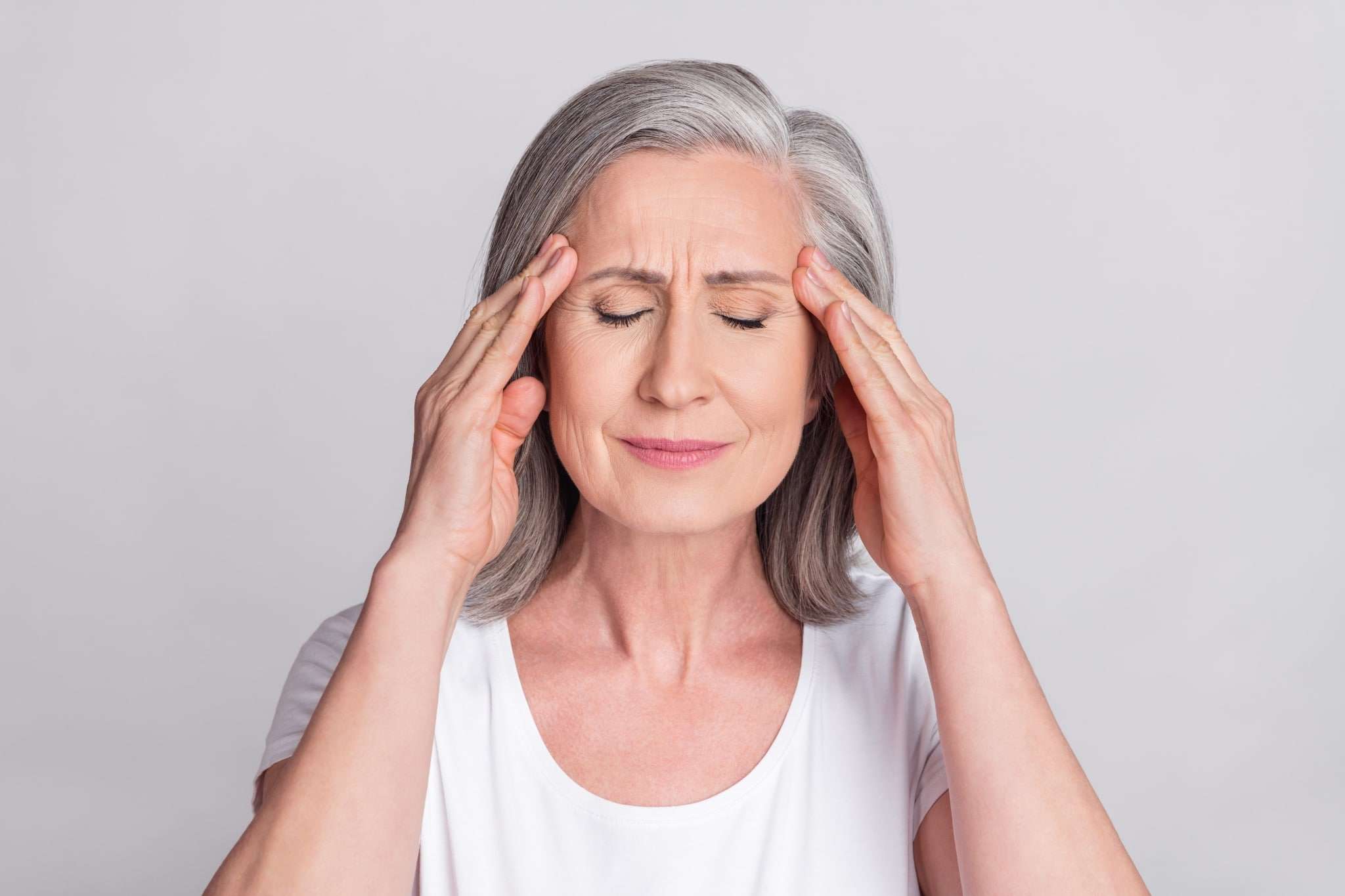 An elderly woman holding her temples during a migraine.
