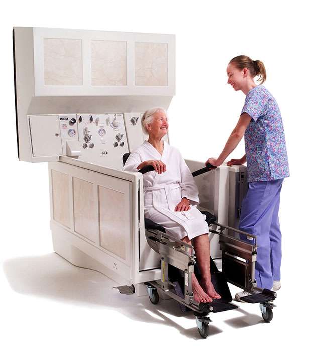 A caregiver helping an elderly patient into an Apollo Bathing system with a transfer.