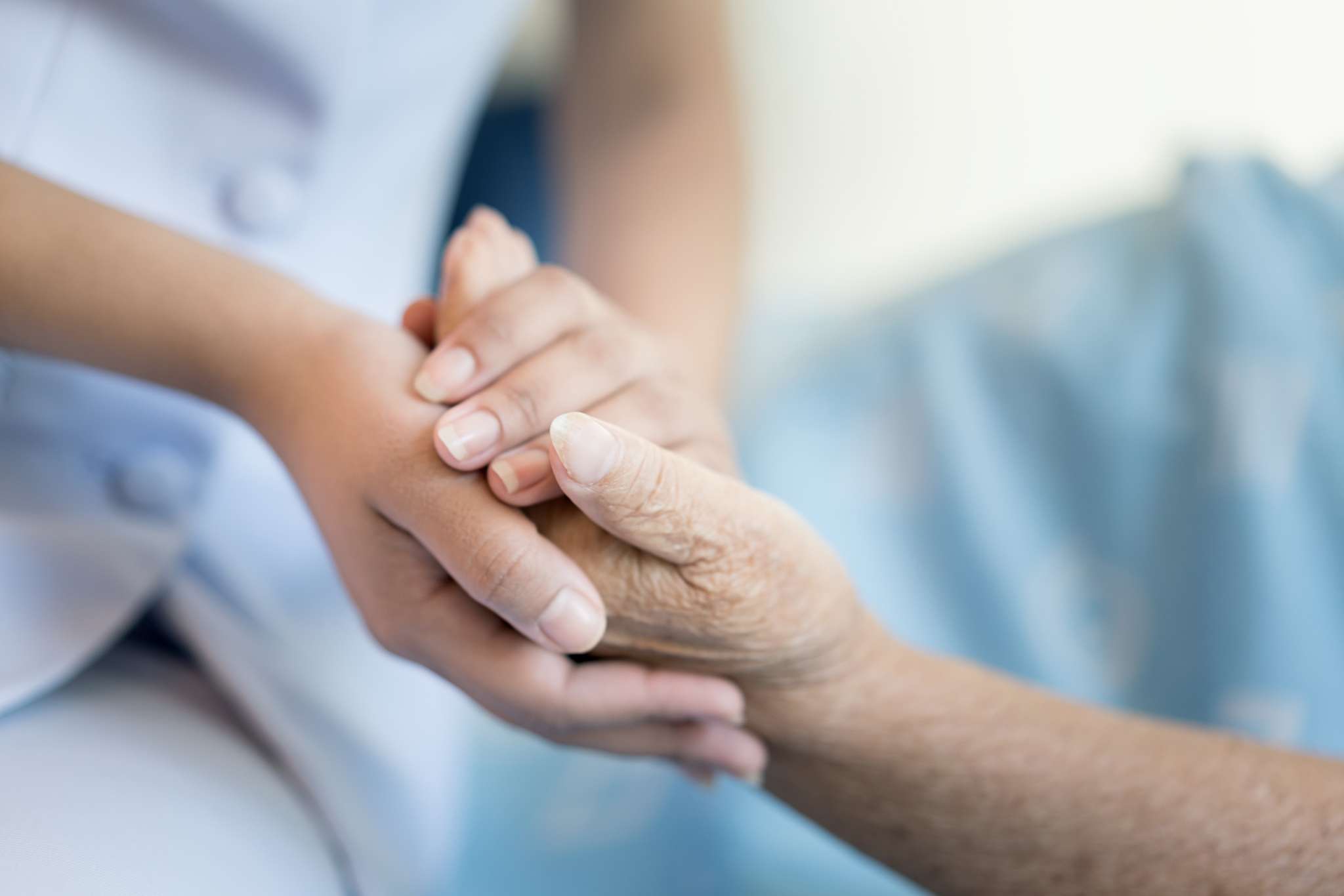 A long-term caregiver holding the hand of a patient.