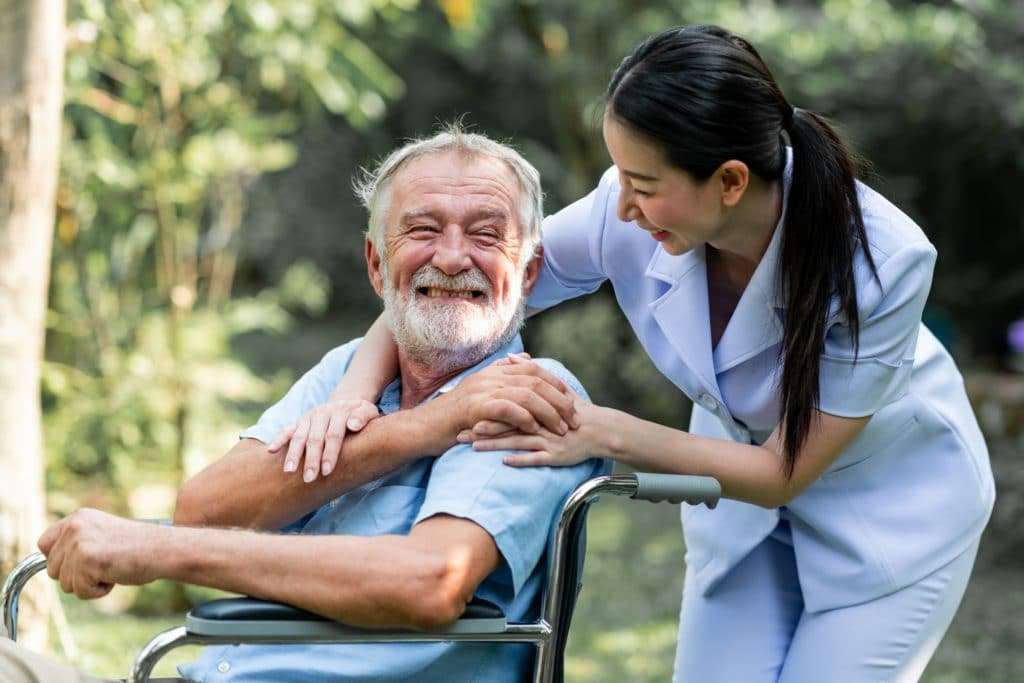 A senior man smiling in a wheelchair next to his caregiver.