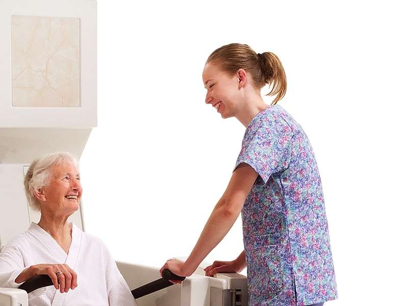 Top 8 Features to Look For in Tubs for Seniors 7 A caregiver helping a patient into a tub with a water reservoir tub accessory.